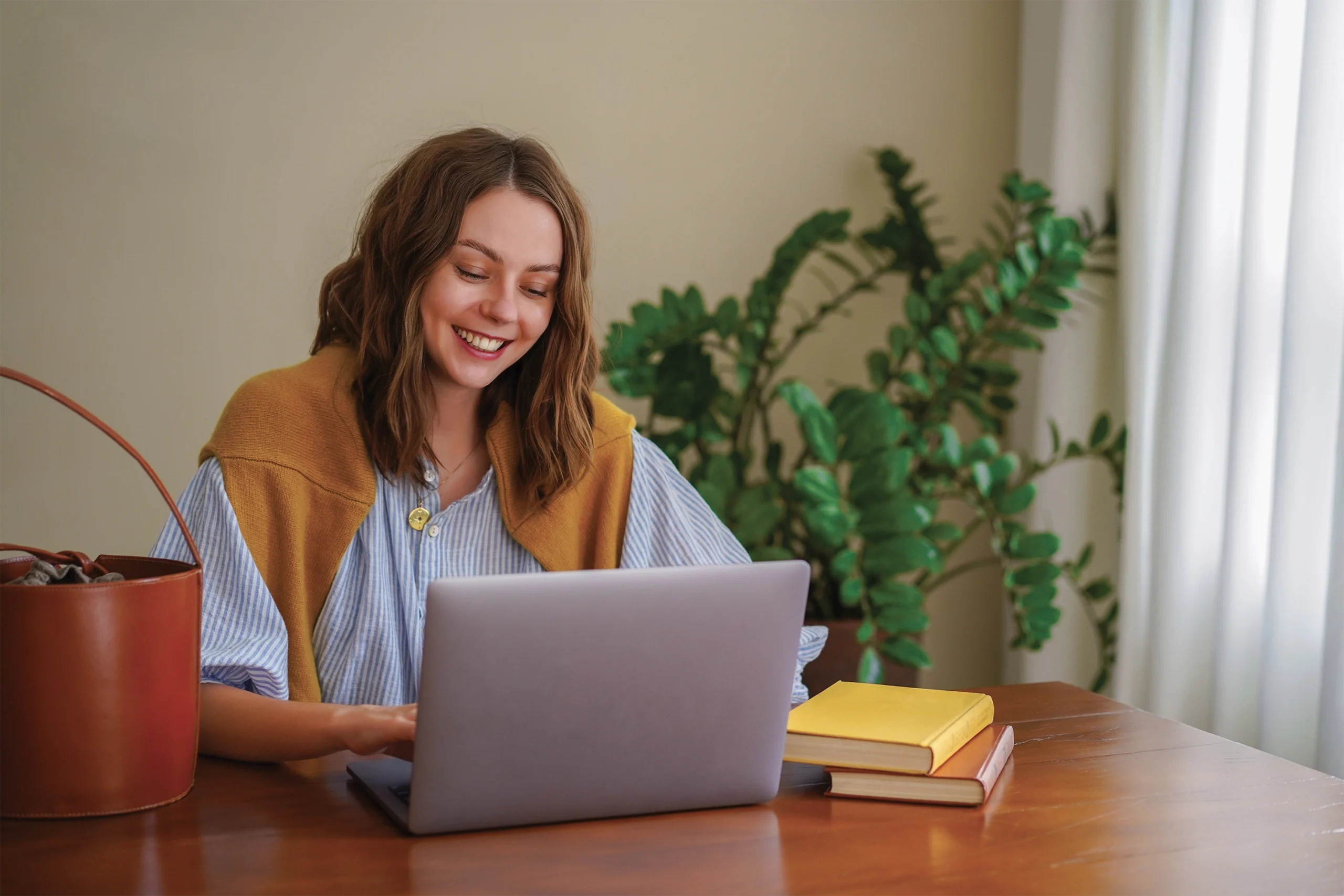 Jeune fille ultra souriante, assise à une table, travaillant sur son ordinateur, regardant son écran